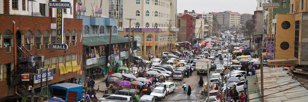 A busy high stree in Vietnam showing shops with market stall, cars, vans and people crowded in the main street.