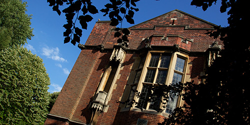 Old red-brick building surrounded by trees on a sunny day. 