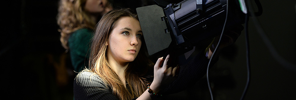 Student carefully adjusting professional lighting equipment. 