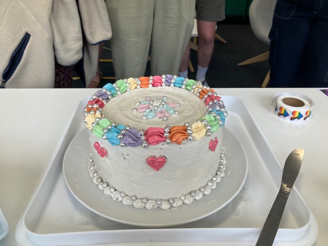 A white chocolate cake decorated with rainbow coloured icing and hearts.