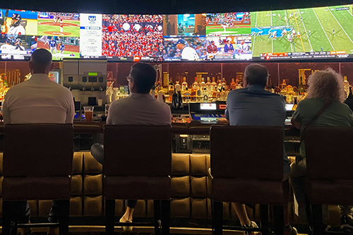 A group of people sitting at a bar watching sport on TV