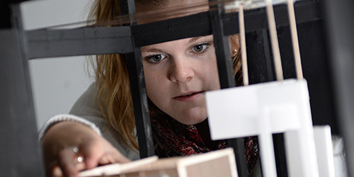 A white woman looks and puts her hand into a model theatre set.