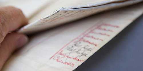 A hand folding a folded piece of paper with illegible red and black writing on it.